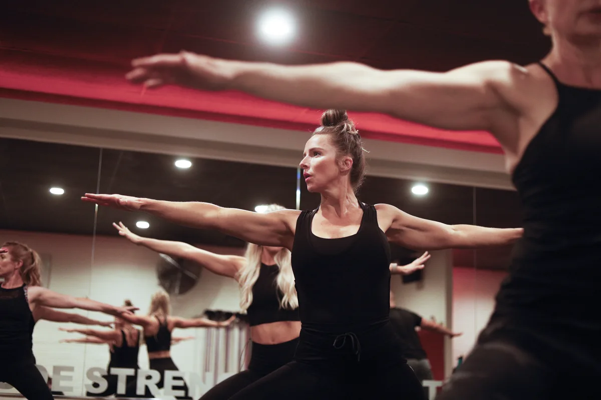 An Obsidian® SOUL class holding a wide-armed standing pose in front of the studio mirrors